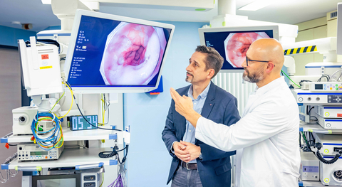 Dr. Viktor Rempel und patient Andreas Nickel stehen in einem Endoskopieraum und sehen sich Herrn Nickels Endoskopie-Aufnahmen seines Speiseröhrenkrebses auf einem Bildschirm an.
